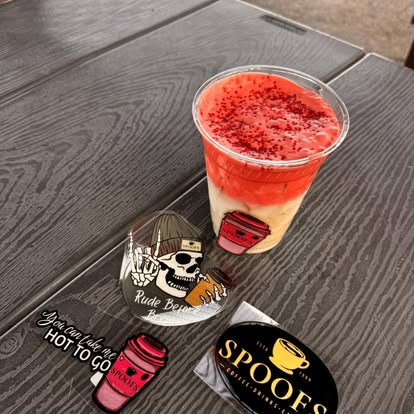 A berry-red drink with Spoof's stickers and lid on the table